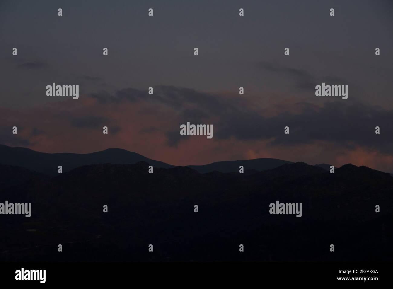 Mountain range blue shapes at sunset under a violet cloudy sky at the end of day Stock Photo