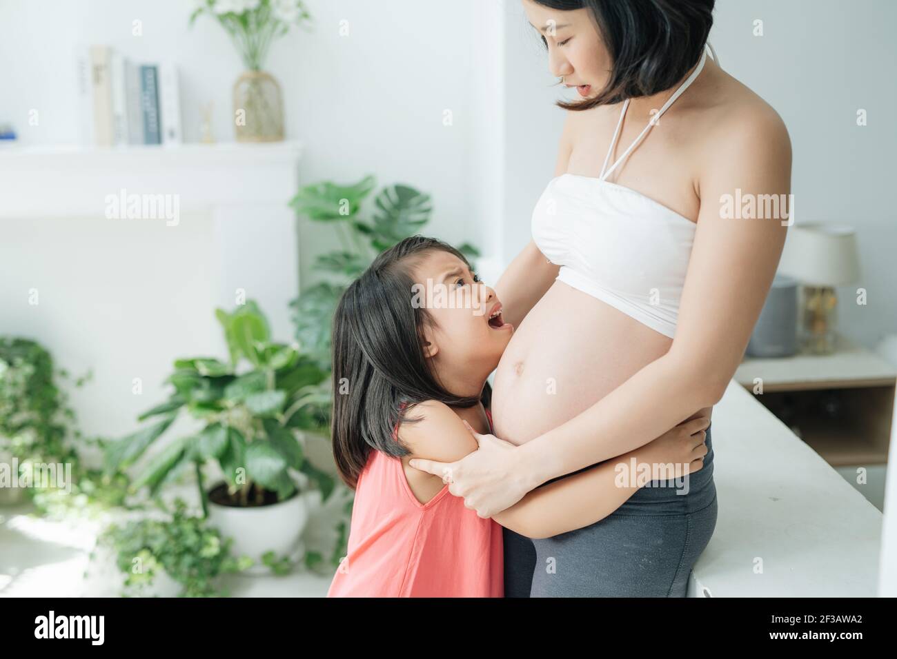 I don't want brother. Sad little daughter looking at her pregnant mom belly, child crying for not wanting sibling, family issue, close up Stock Photo