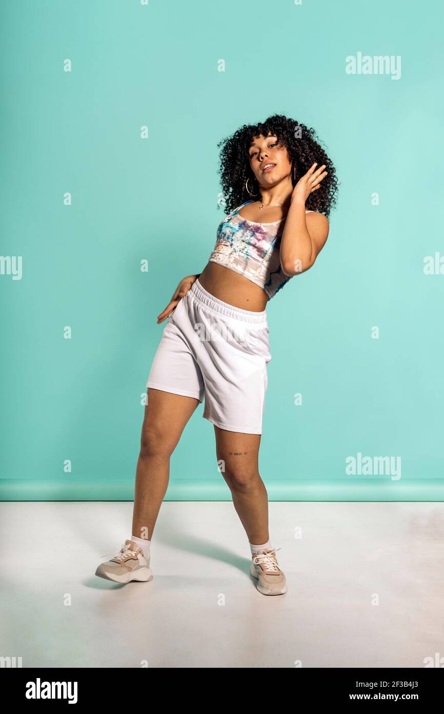 Stock photo of beautiful african woman with curly hair dancing in studio shot against blue background. Stock Photo