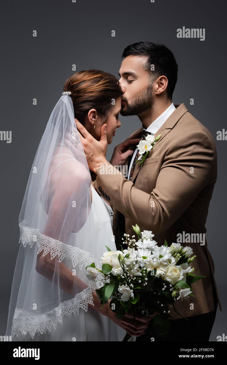 muslim man kissing bride holding wedding bouquet isolated on grey Stock Photo