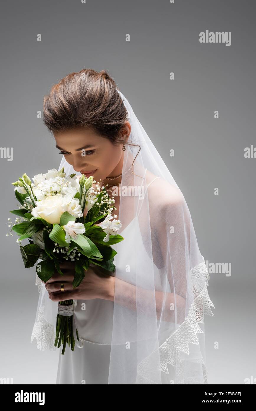 Brunette bride smelling wedding bouquet isolated on grey Stock Photo