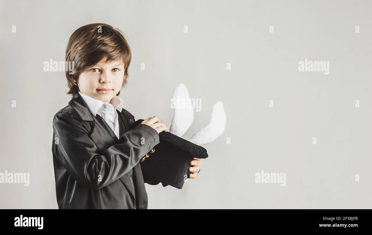 Young magician hiding a toy bunny in his top hat over grey background. Magical performance concept Stock Photo