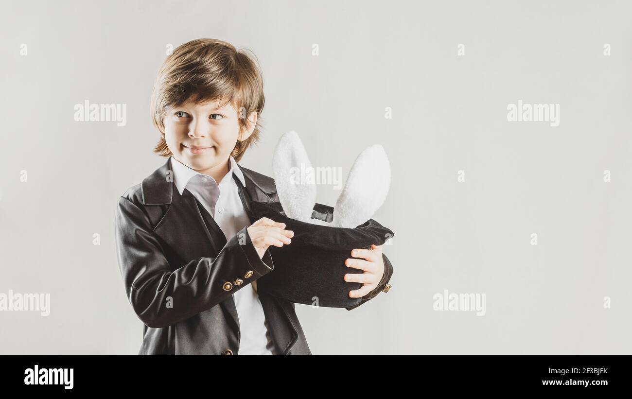 Young magician hiding a toy bunny in his top hat over grey background. Magical performance concept Stock Photo