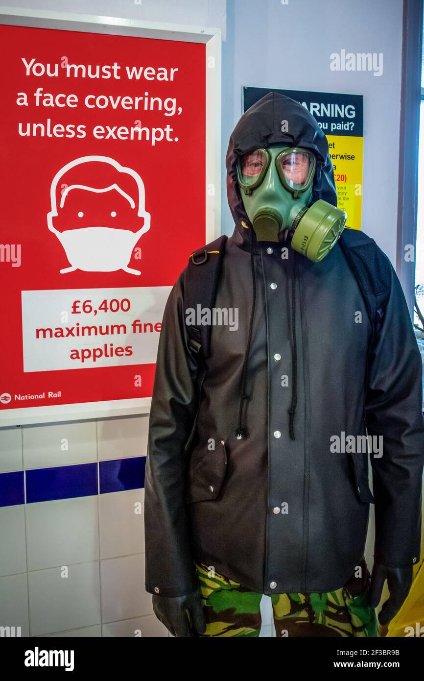 Man in Gas Mask in Chislehurst Station in front of You must wear a face covering unless exempt sign, protecting himself from the pandemic Stock Photo