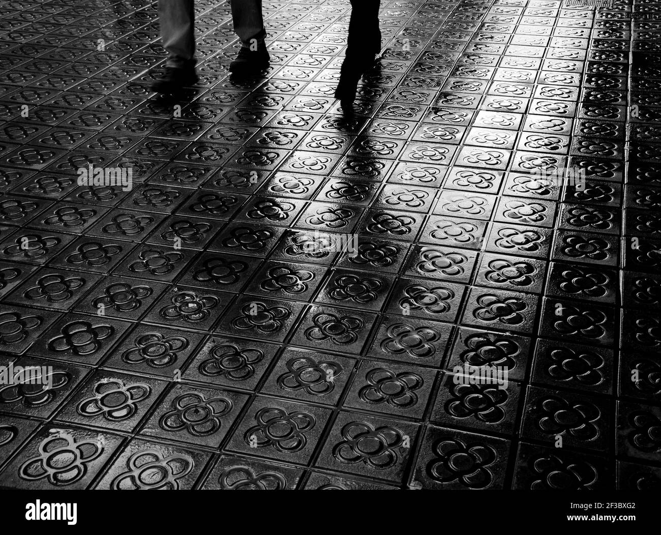 Barcelona, Spain. Couple legs and their reflection on wet flower street paving. Romantic vacation background. Black and white photo. Stock Photo