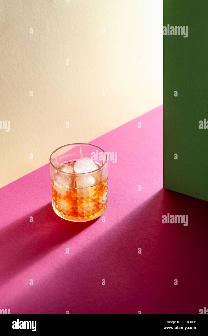 Glass with Whiskey and Ice Cube on Table with Hard Shadows. Modern Isometric Style. Creative Concept. Stock Photo
