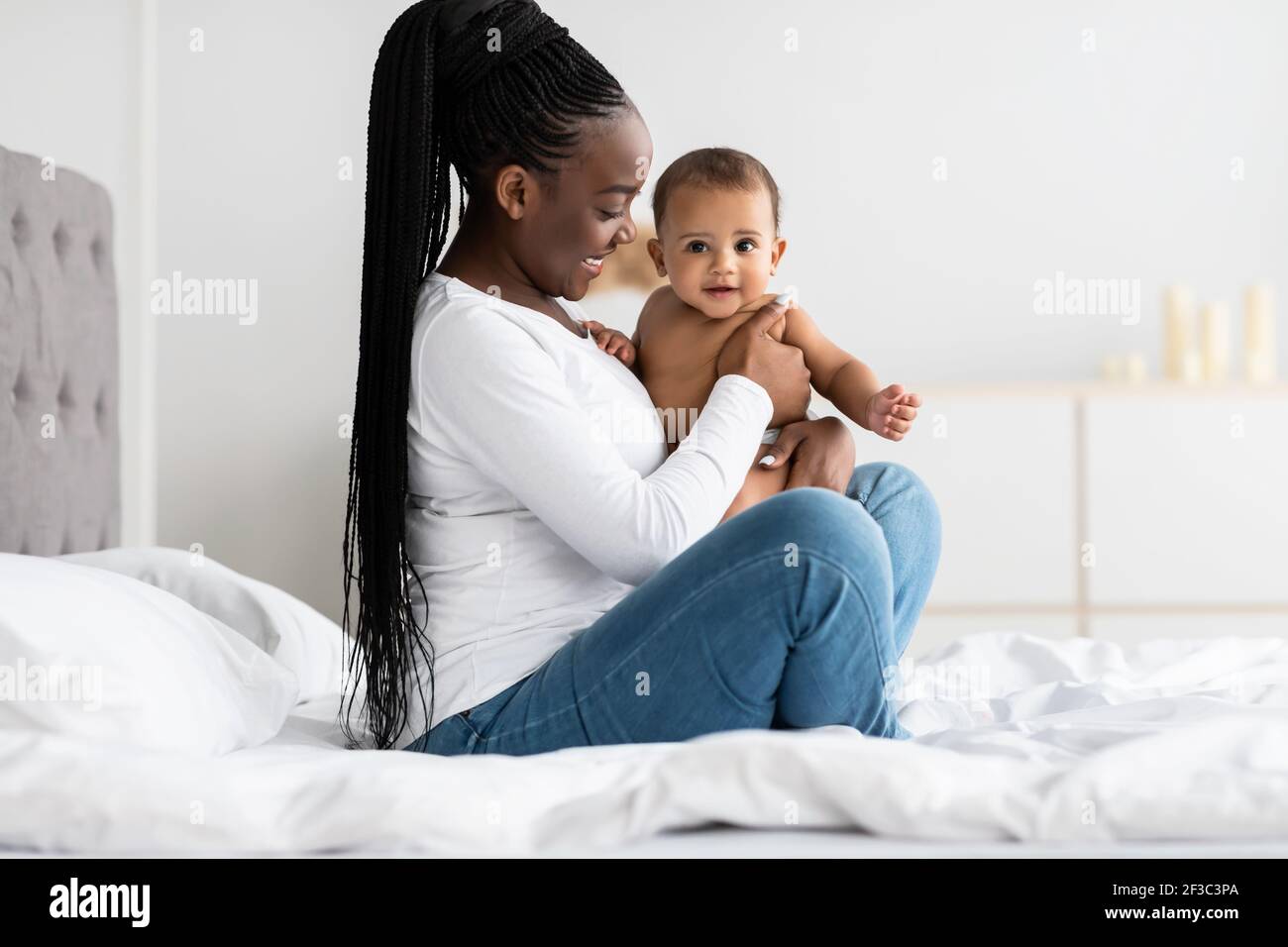 Cute little African American baby sitting on bed with mother Stock ...