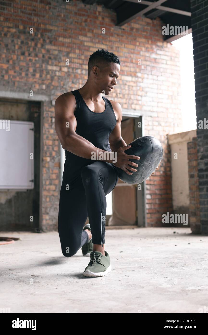 African american man exercising in warehouse doing lunges holding medicine ball Stock Photo