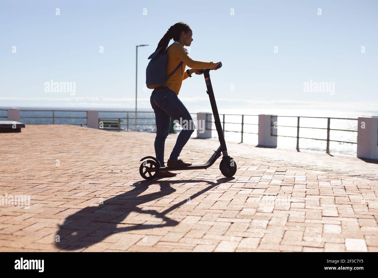 Smiling african american woman admiring sea view with scooter on promenade by the sea Stock Photo