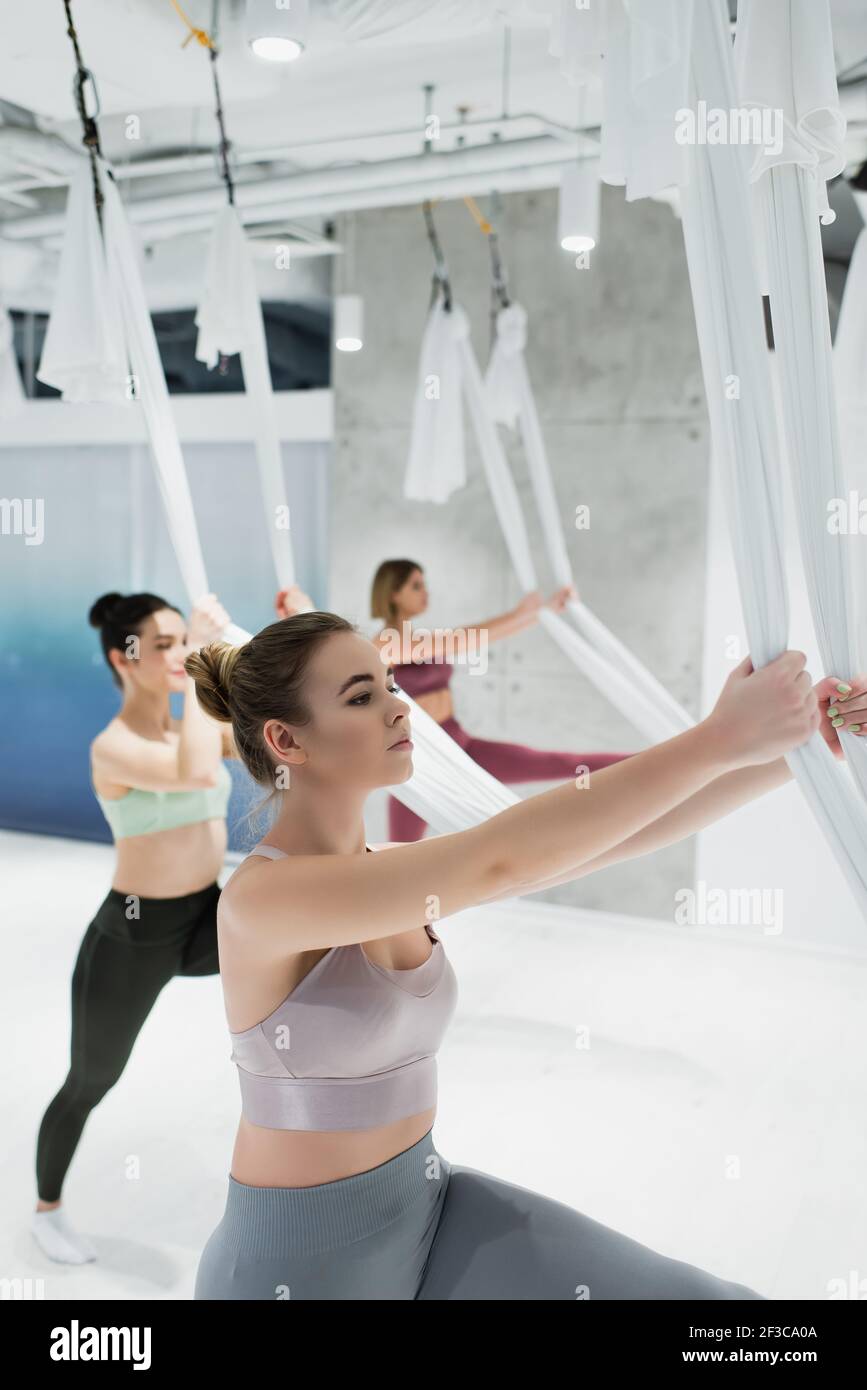pretty women warming up with fly yoga hammocks in fitness center, blurred background Stock Photo