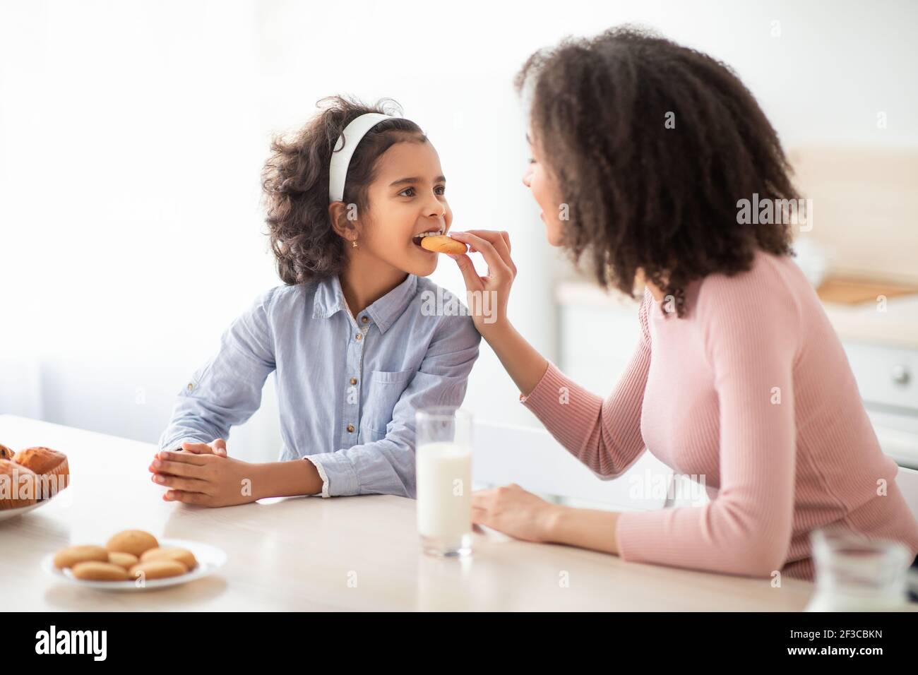 Cheerful african american woman feeding girl with cookie Stock Photo