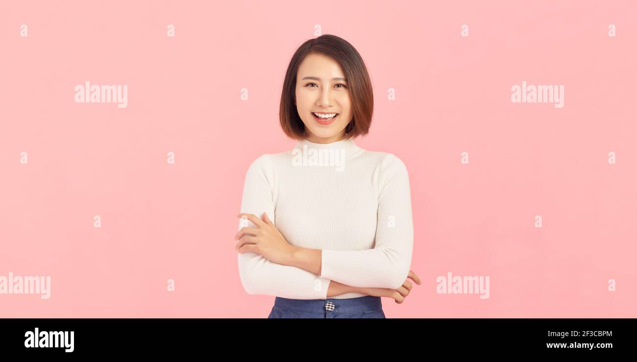 Confident business expert. Beautiful young woman in smart casual wear keeping arms crossed and smiling while standing against pink background Stock Photo
