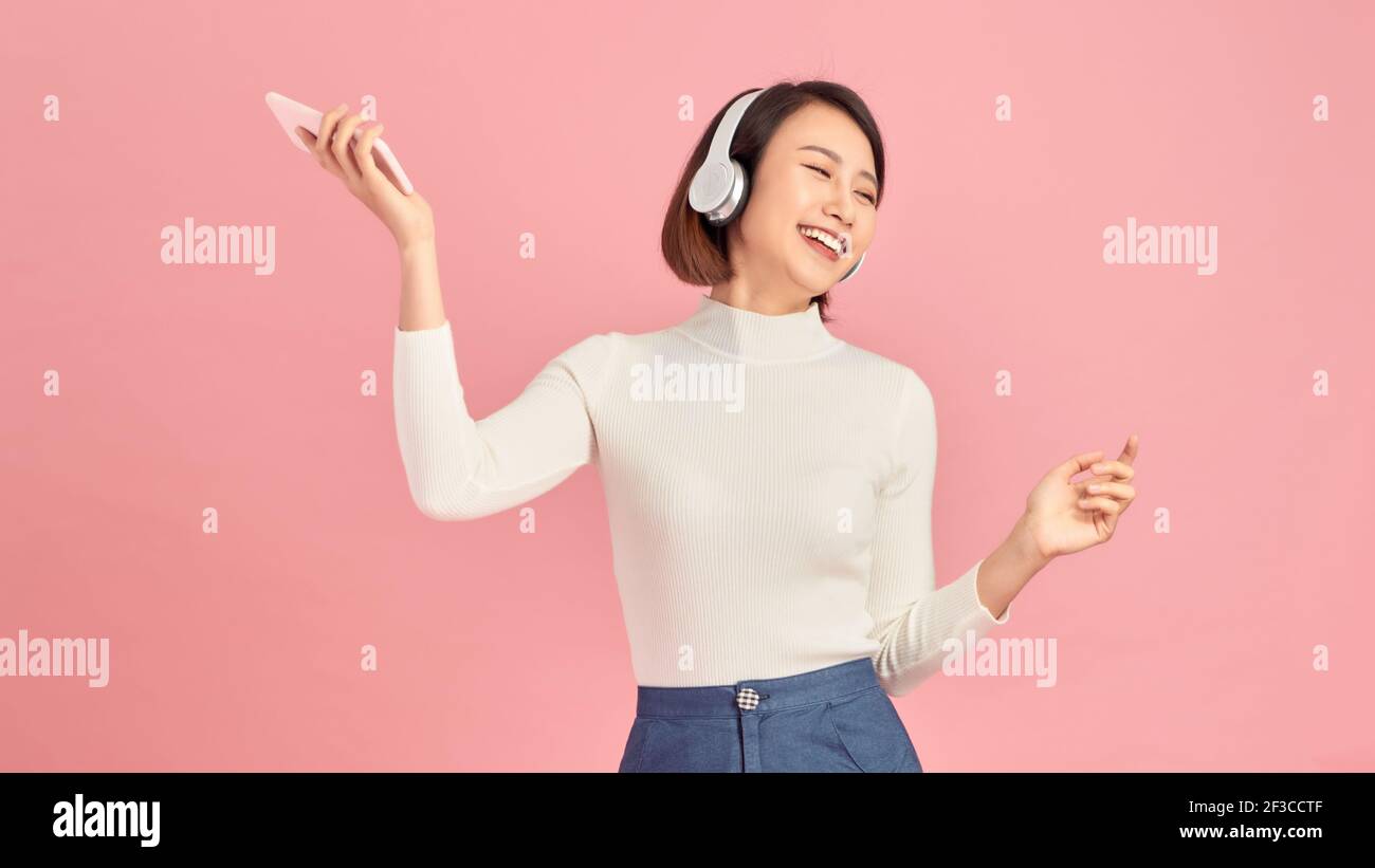 Happiness Asian smiling young woman wearing technology wireless headphones for listening the music via smart mobile phone Stock Photo