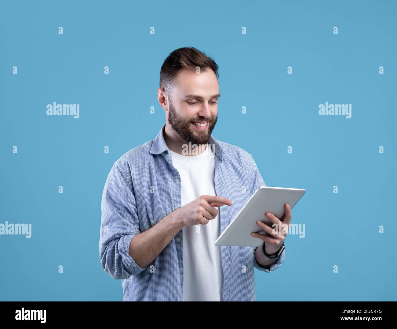 Joyful bearded man using tablet computer for online work or studies on blue studio background Stock Photo