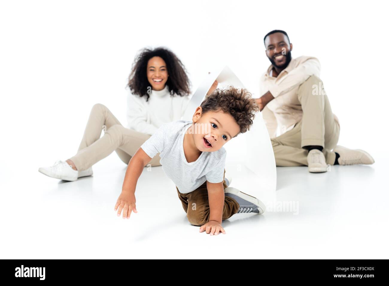 african american boy crawling under paper roof near cheerful parents on blurred background on white Stock Photo