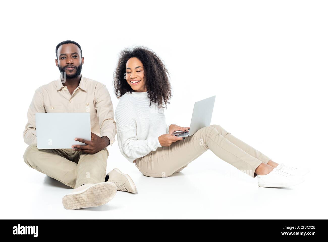african american man looking at camera near curious wife looking at his laptop on white Stock Photo