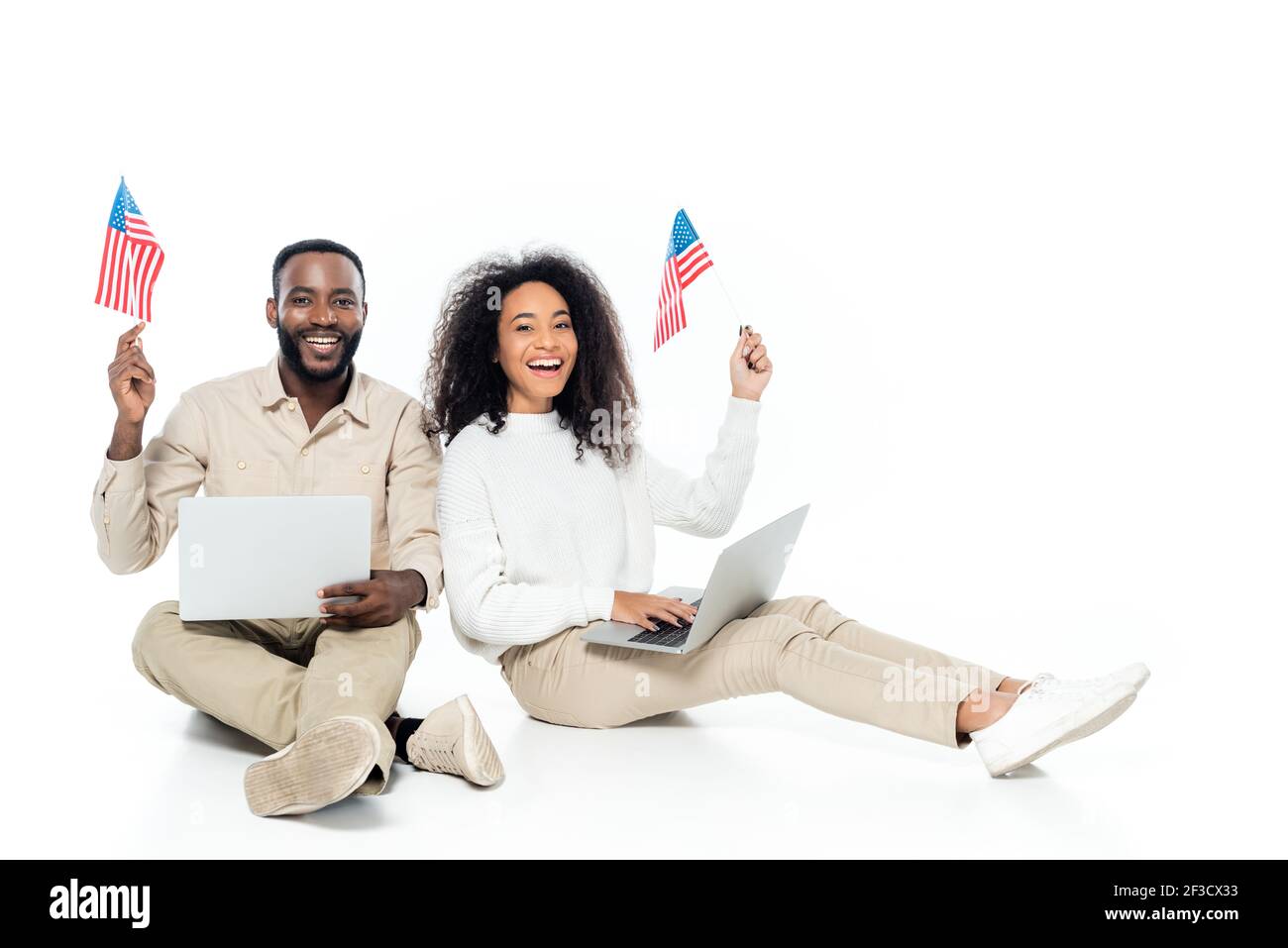 Happy African American Couple Holding Small Flags Of Usa While Sitting With Laptops On White