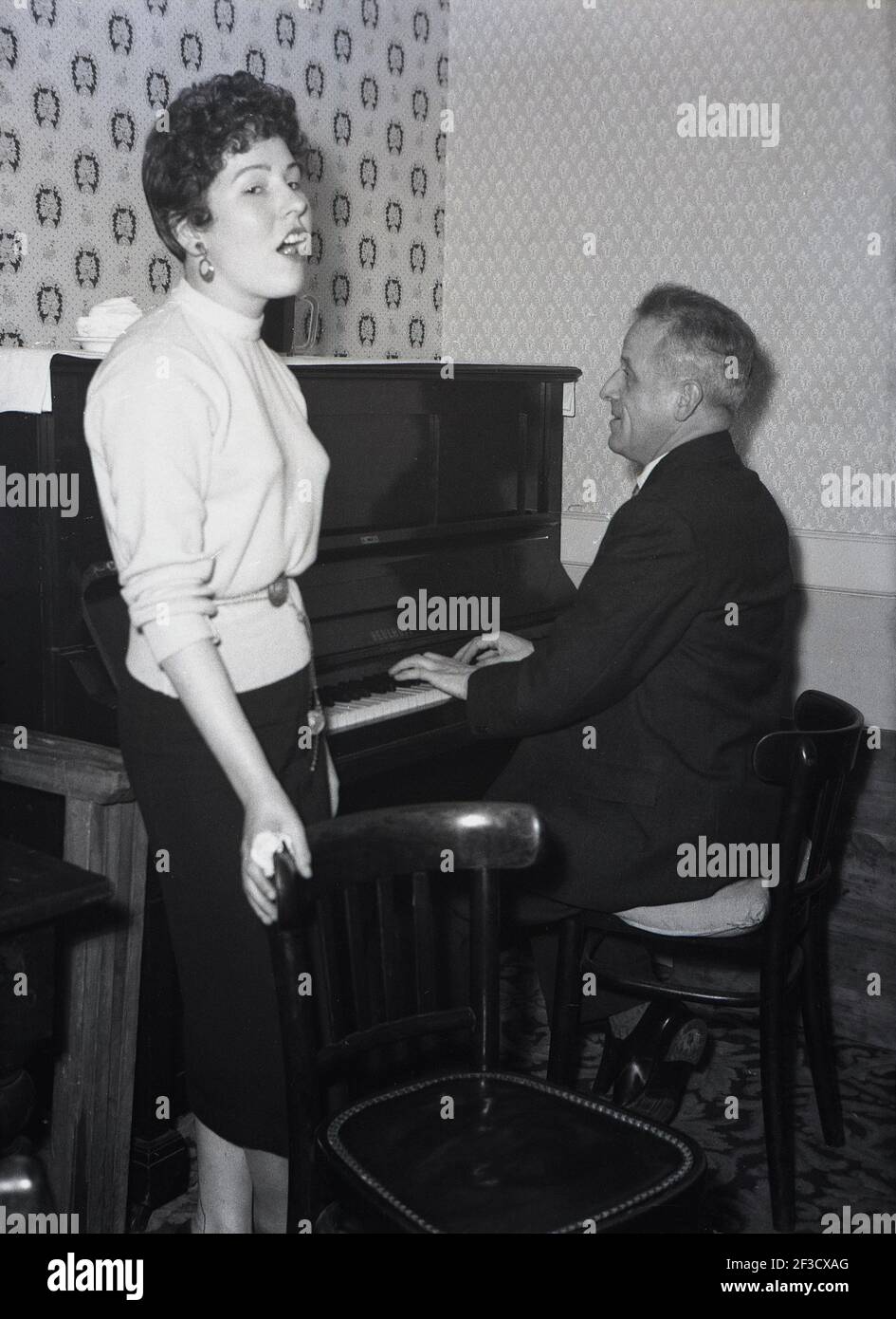 1957, historical, inside a hotel lounge bar, a young lady standing, singing a song, as a mature gentleman plays the piano, Leeds, England, UK. Stock Photo