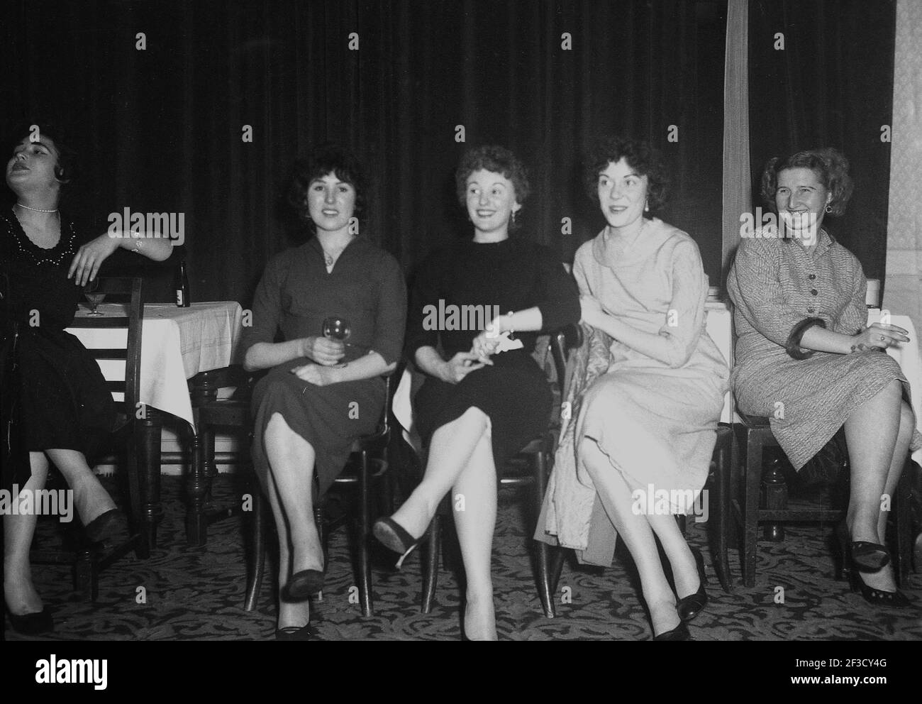 1957, historical, evening time and four young ladies in the female fashions of the era sitting on chairs in a function room of the Victoria hotel at an office party, perhaps by the amusing look on their faces, watching others dance, Leeds, England, UK. Stock Photo
