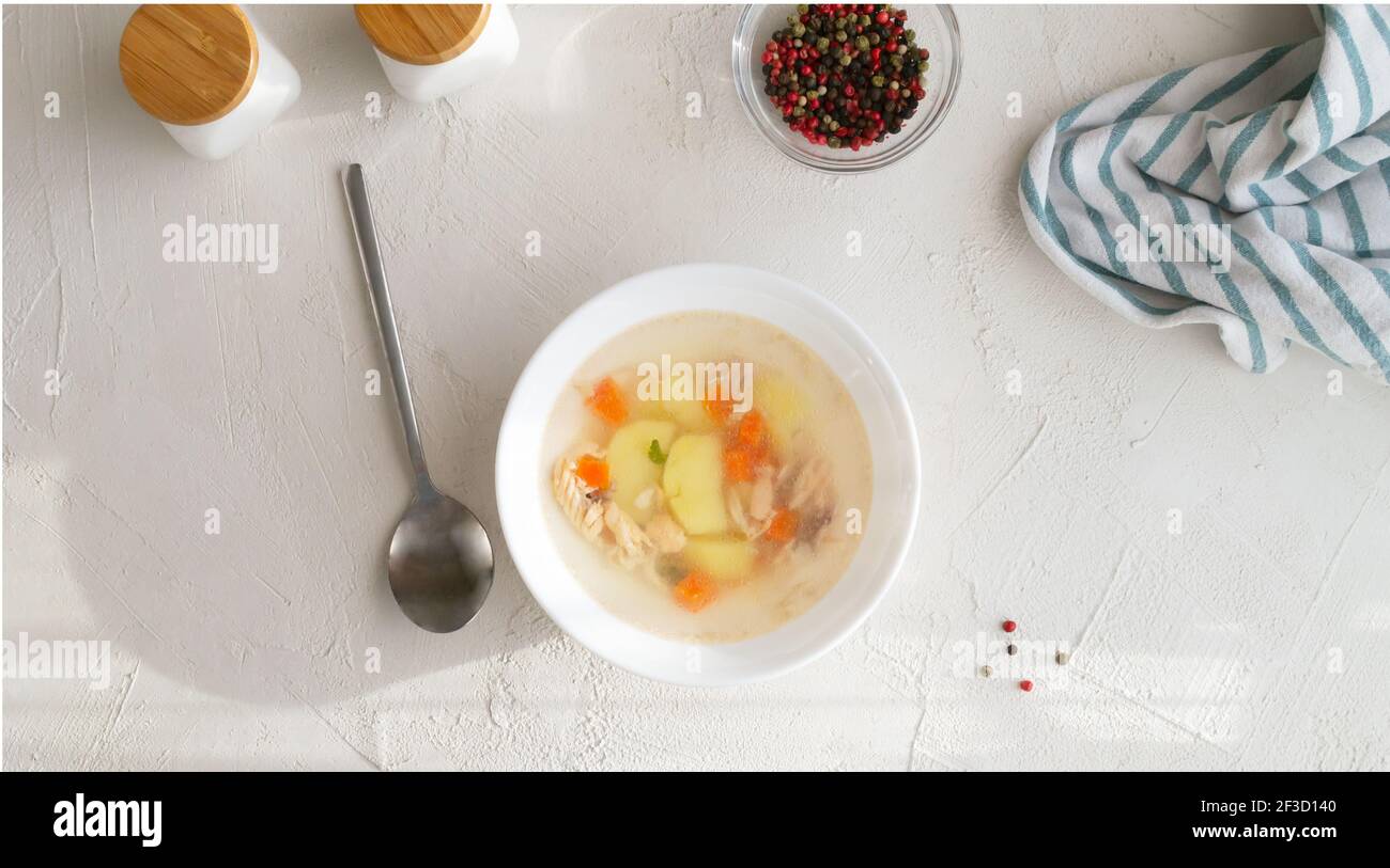 Transparent fish soup with vegetables in a white bowl on a white plate. Healthy nutrition concept. Top view. Horizontal orientation. Stock Photo