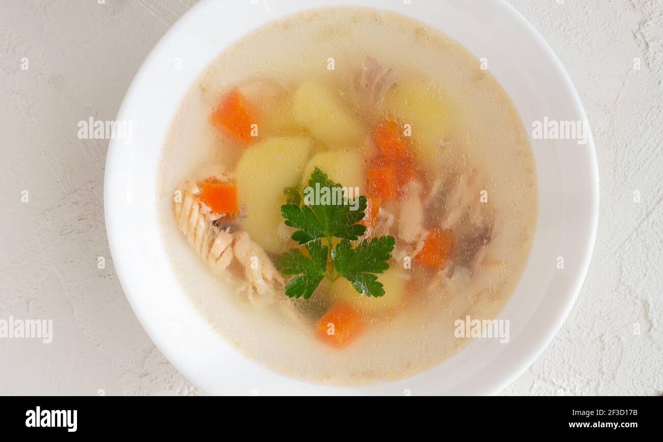 Clear fish soup with pieces of vegetables and percussion in a white bowl on a white plate. Healthy food concept. Close-up. Horizontal orientation. Stock Photo
