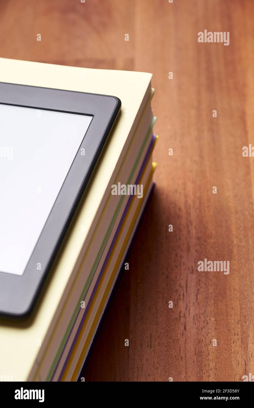 Electronic reader with blank screen on a pile of books on a wooden desk