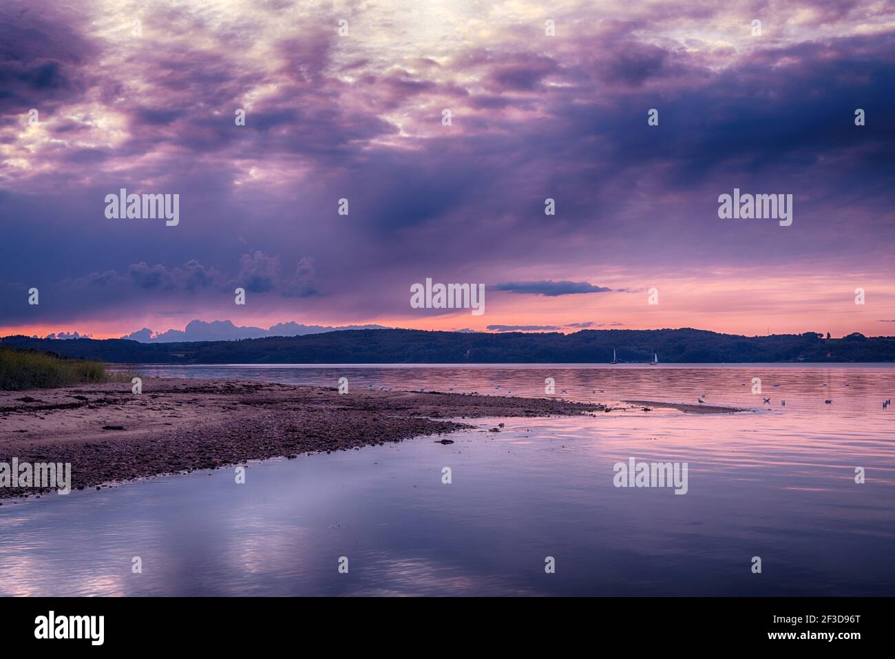 Purple sunset over Vejle Fjord in Denmark. Calm surface waters, surrounded by low forested hills. Beautiful landscape of the Jutland Peninsula. Stock Photo