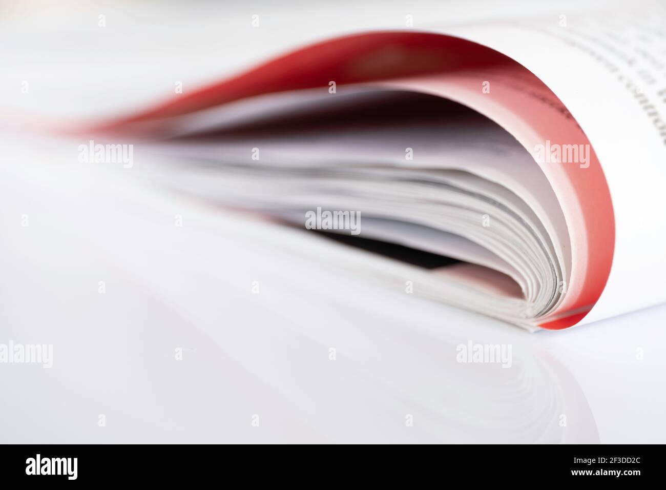 Folded magazine with red page reflected on a white surface with shallow depth of field Stock Photo