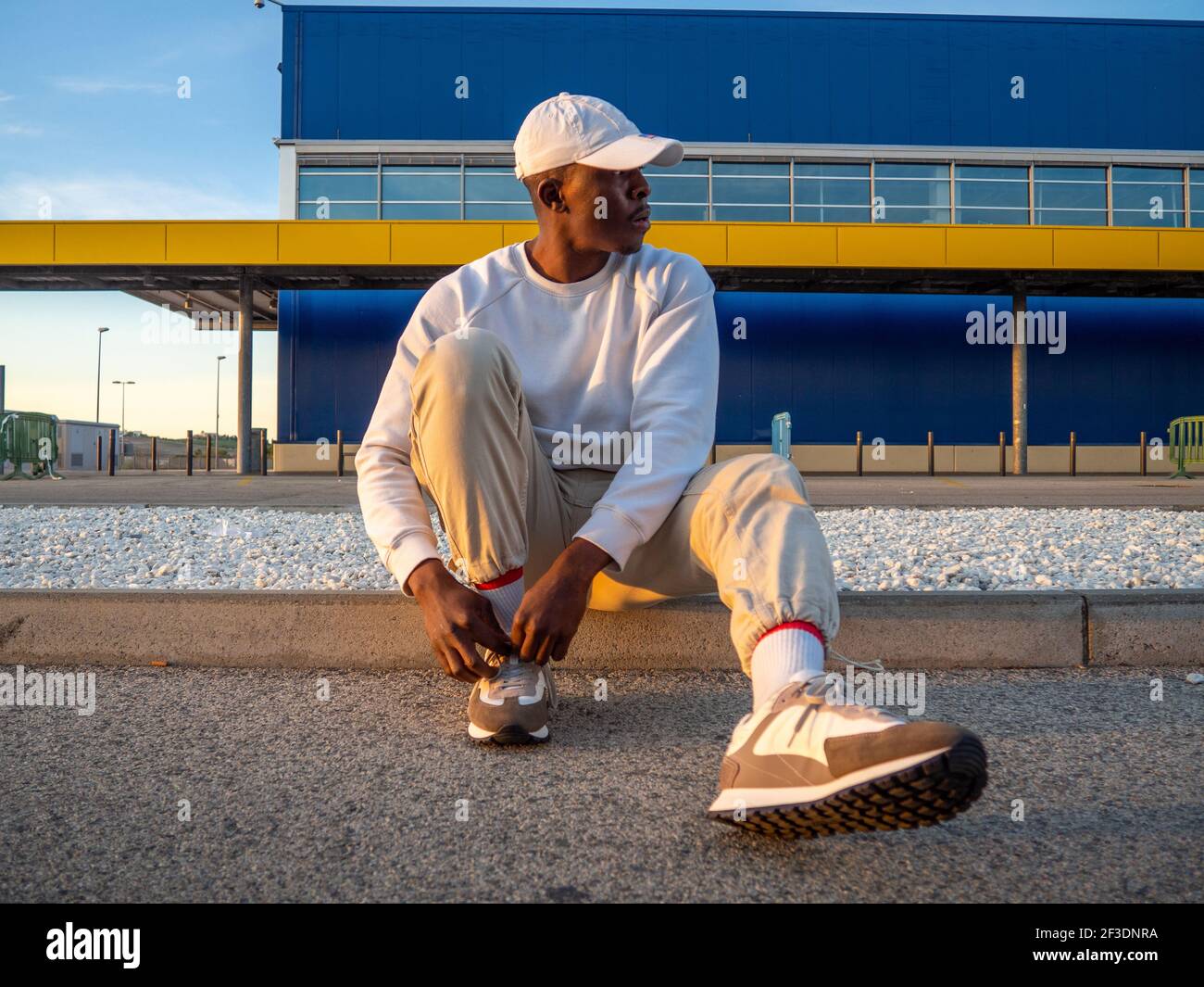 A black Spanish male tying shoelaces while sitting on a curb Stock
