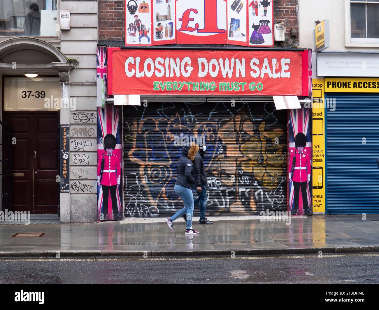 graffiti covered closed shut closing shop on Londons Oxford Street, with closing down sale sign and shoppers wearing ppe masks during England Covid-19 coronavirus lockdown Stock Photo