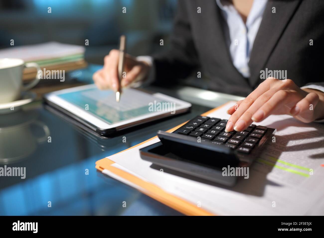 Close up of a businesswoman hands using tablet and calculator in the night at homeoffice Stock Photo