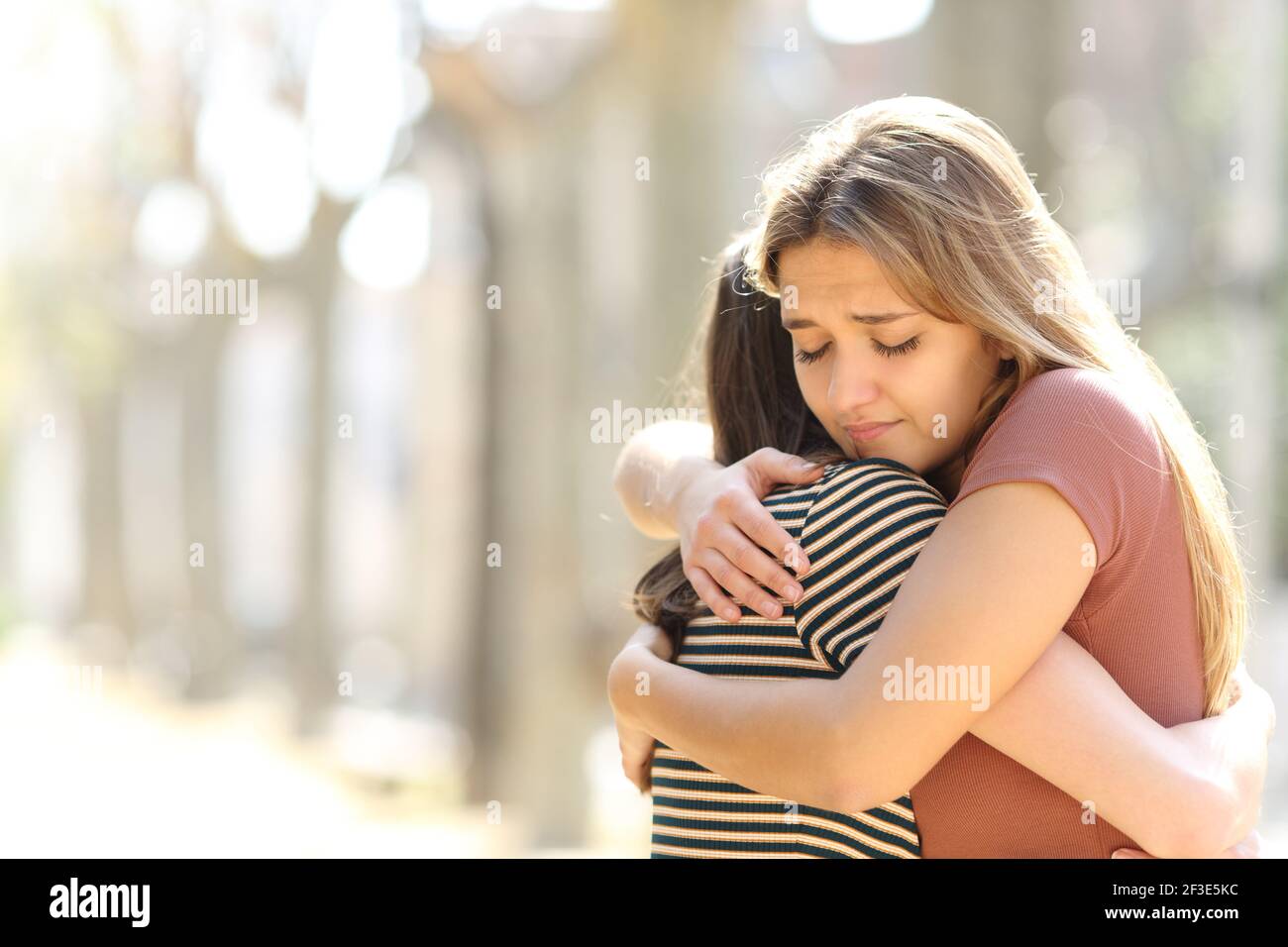 Regretful woman embracing a friend reconciliating in the street Stock Photo
