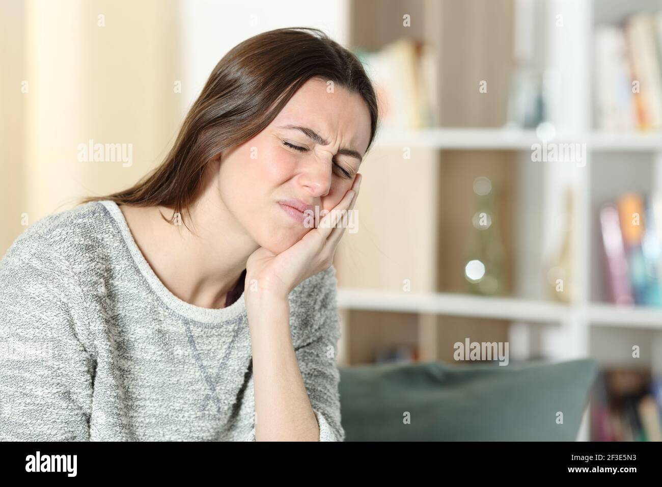Stressed woman suffering toothache complaining touching cheek on a couch at home Stock Photo