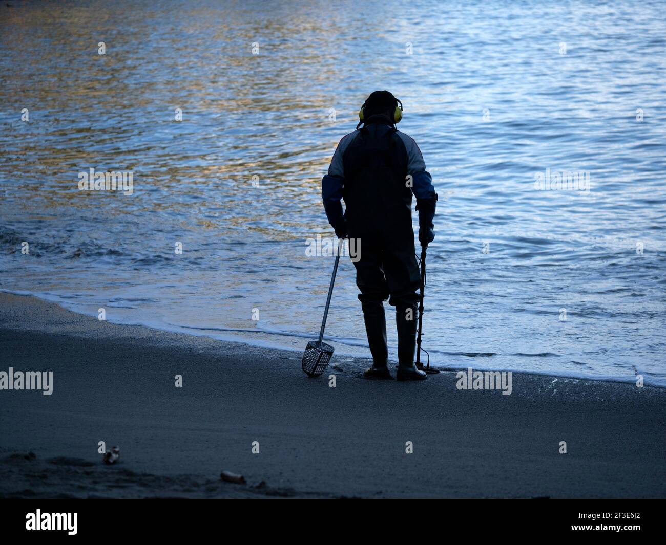 man searching with metal detector on the beach at sunset Stock Photo ...