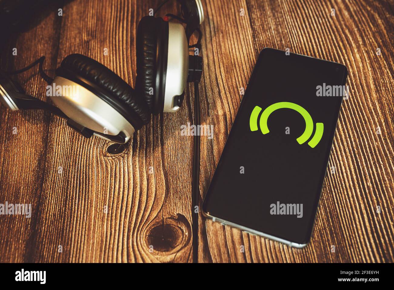 Smartphone with green Beatport logo on dark screen with headphones on wooden background. Online music store Stock Photo
