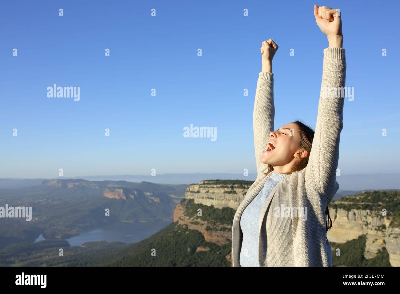 Excited casual woman celebrating vacation raising arms and screaming in the mountain Stock Photo