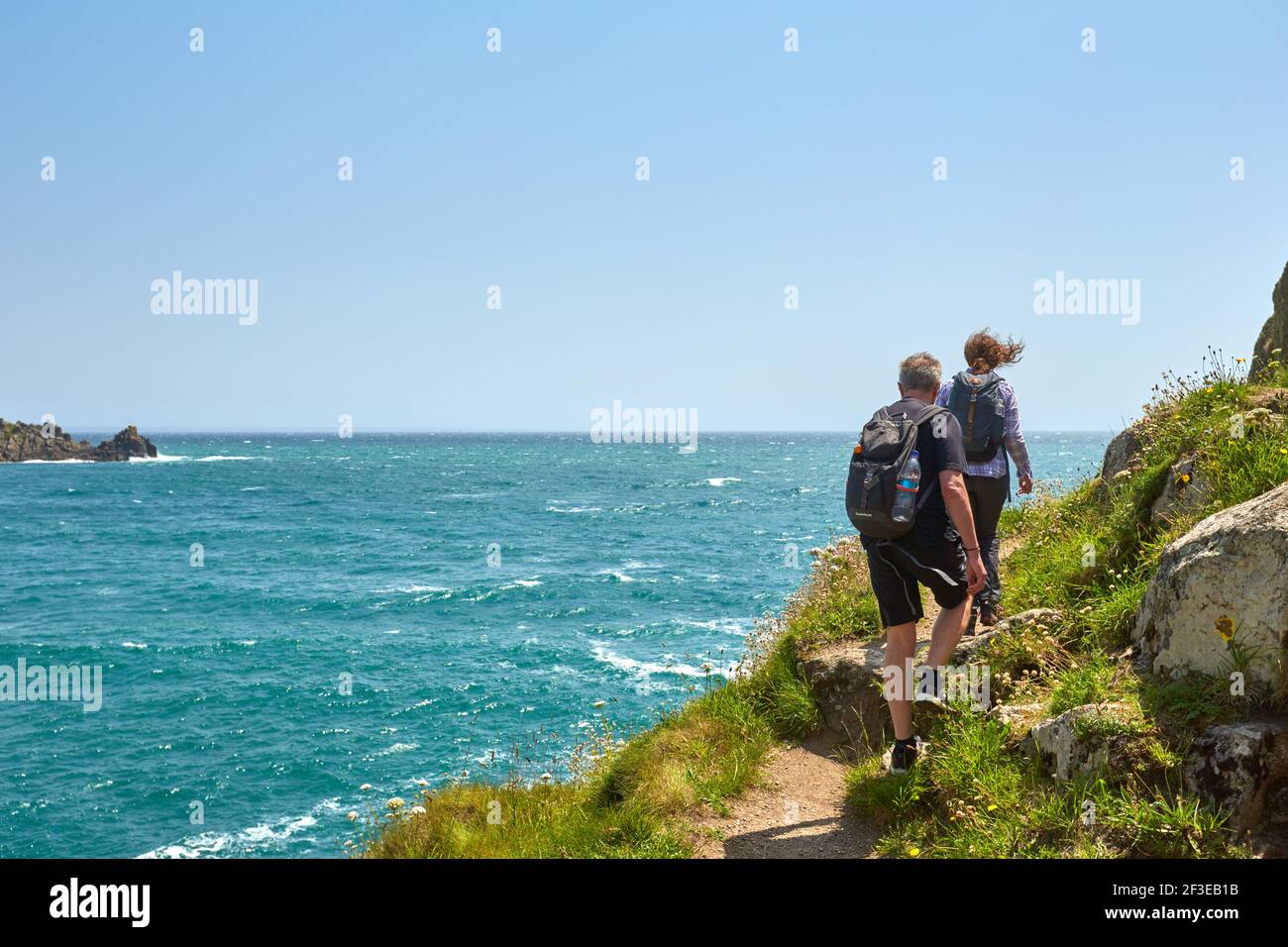 Man and woman walk along the coast path in  Lamorna Cove in Cornwall Stock Photo