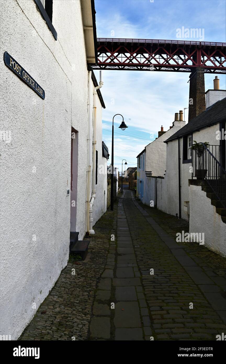 A view along an old cobbled lane and the Forth railway bridge which towers over the historic town of North Queensferry Stock Photo