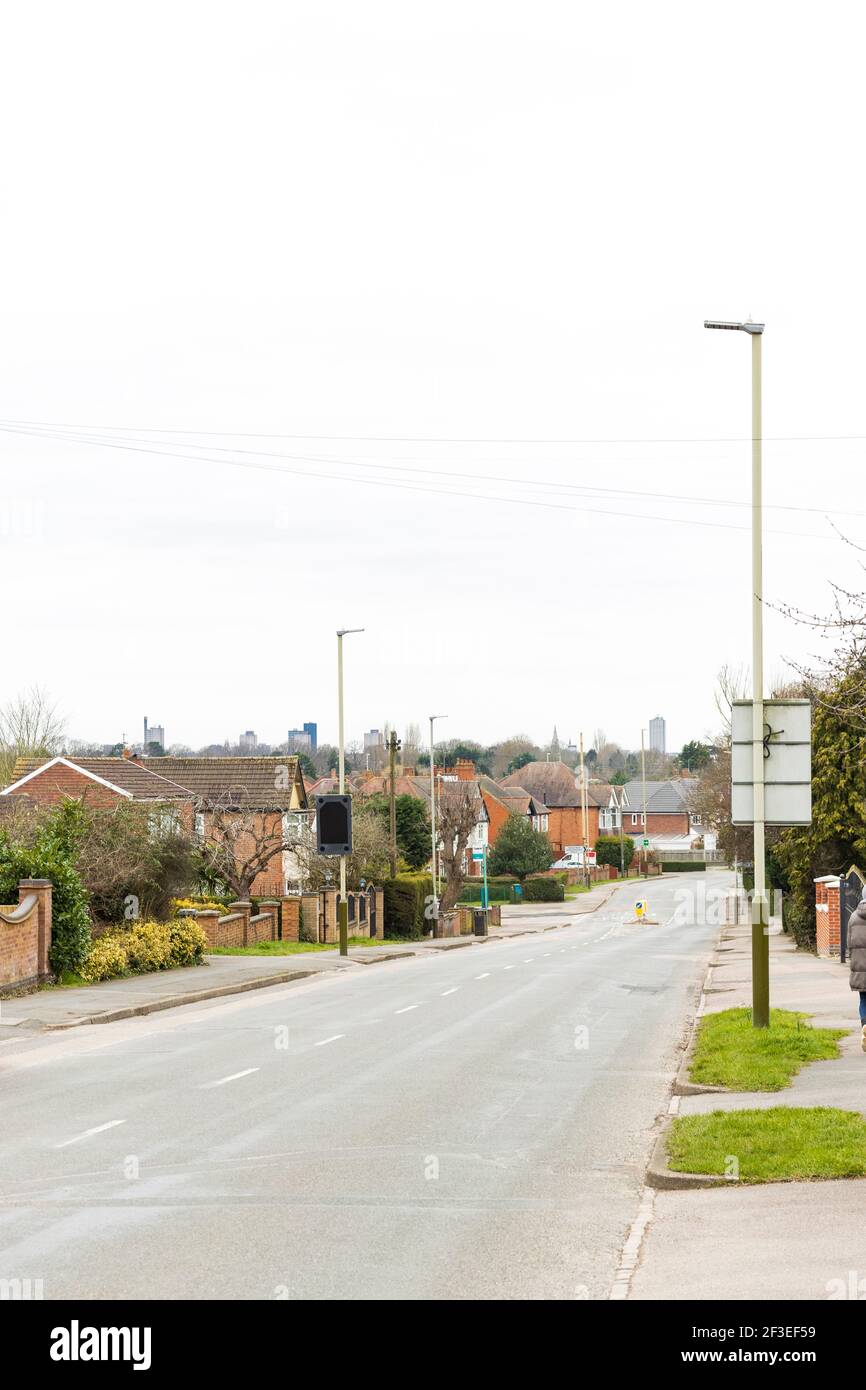 Long suburban road with small pedestrian crossing. Shows houses and pavement either side, with Leicester city skyline in the background. Stock Photo