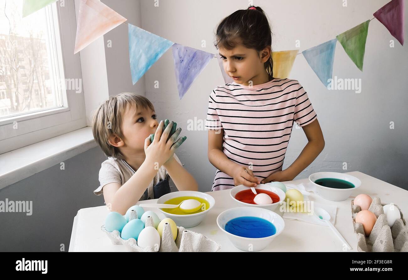 Cute siblings getting ready to Easter celebrate at home. Adorable little girl and her brother dye easter eggs with a colored liquid dye Stock Photo