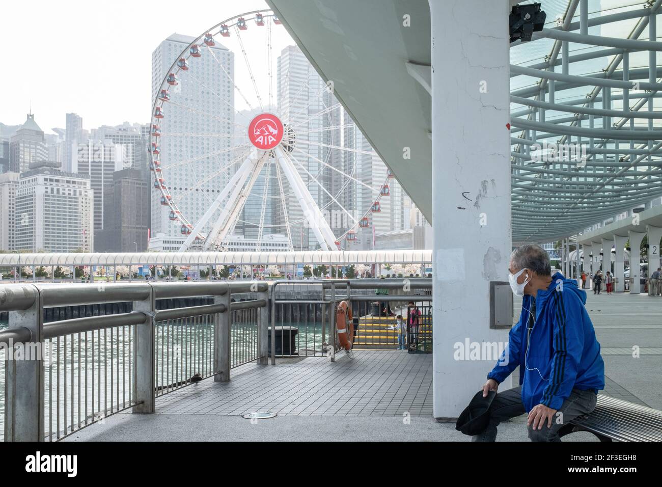 Hong Kong, China. 16th Mar, 2021. A man wearing a face mask as a precaution against the spread of coronavirus sits on the pier in Central district. A series of new coronavirus (COVID-19) cases emerged at major banks and law firms in Central district, the business centre of the city, as Hong Kong reported a spike of new infections. Credit: SOPA Images Limited/Alamy Live News Stock Photo