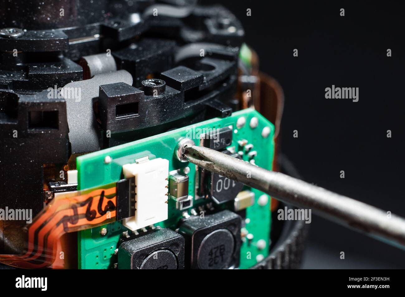 The process of replacing a board with a chip on the lens close-up. Unscrewing the screw holding the control board of the lens Stock Photo