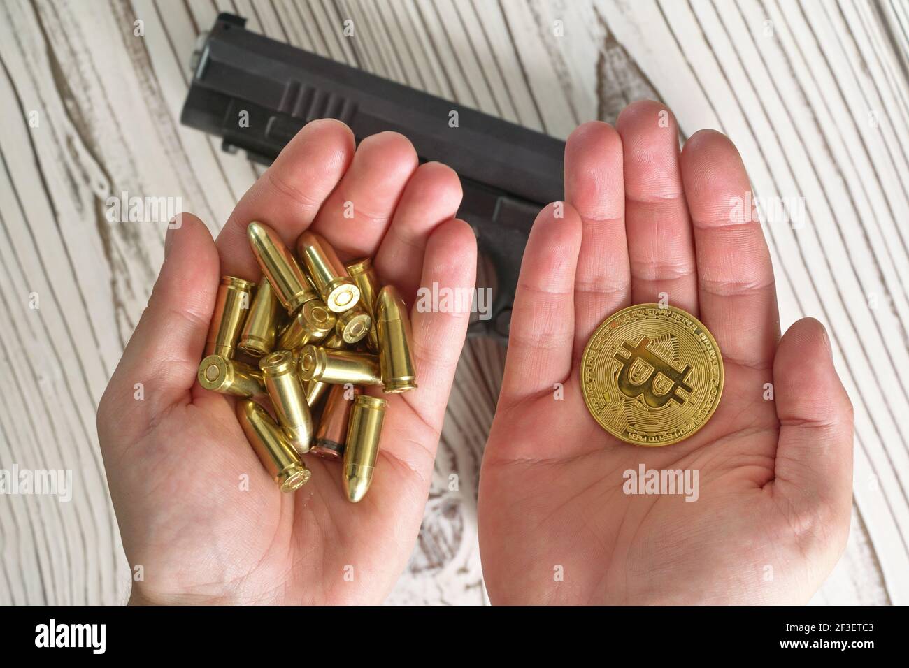 Yellow golden coloured bullets and bitcoin coins in two hands, blurred  wooden desk with black gun under Stock Photo - Alamy