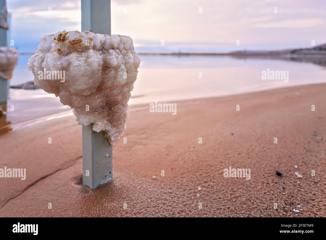 Salt crystals formed on steel bar at the Dead Sea shore, closeup detail, blurred beach and water background Stock Photo