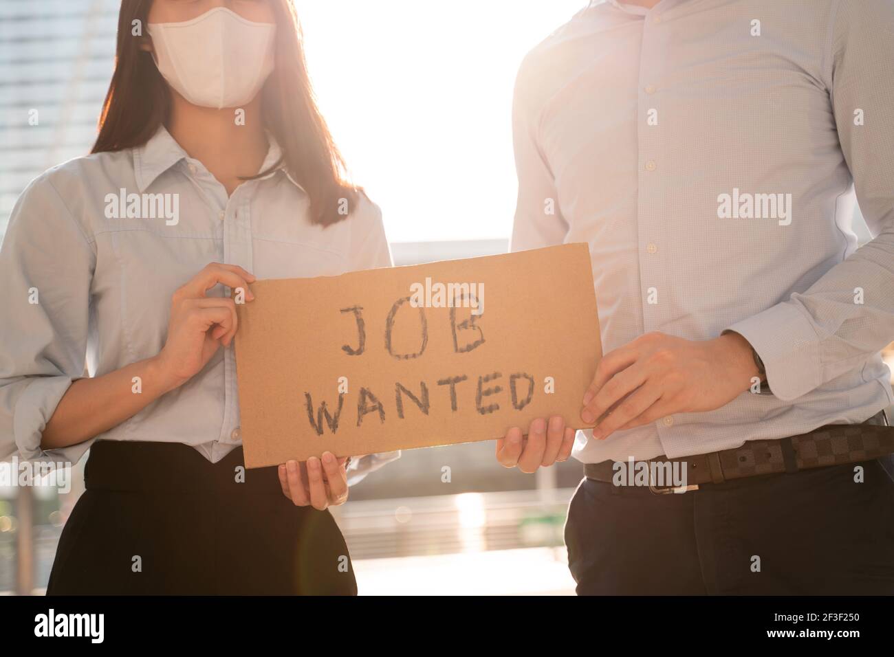 Closeup of hands of young Asian woman and man wearing covid-19 surgical face mask asking for job via message on cardboard placard after losing job due to coronavirus Stock Photo