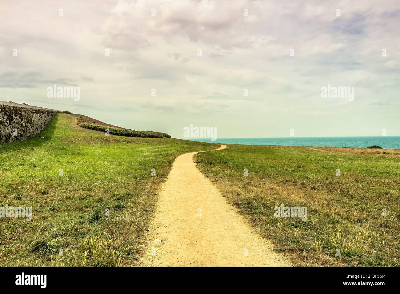 scenery with a winding dirt road heading towards the sea Stock Photo
