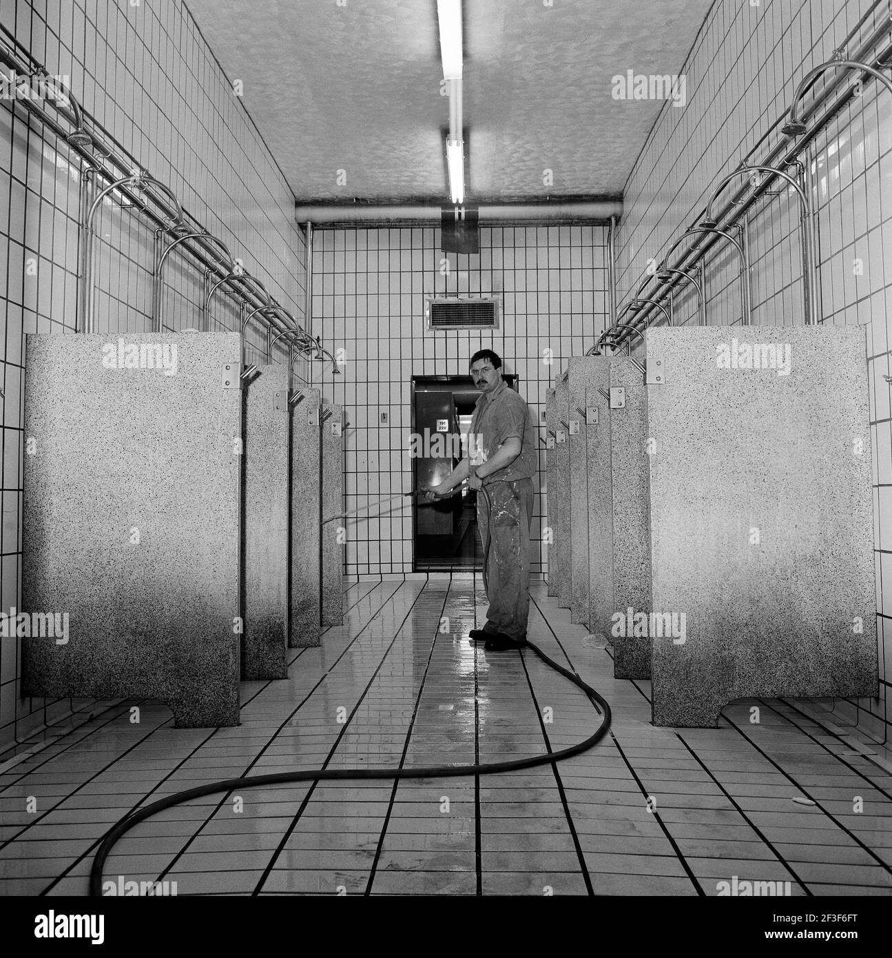 Cleaner cleaning the empty showers with a hosepipe on the surface at Monkwearmouth Colliery Stock Photo