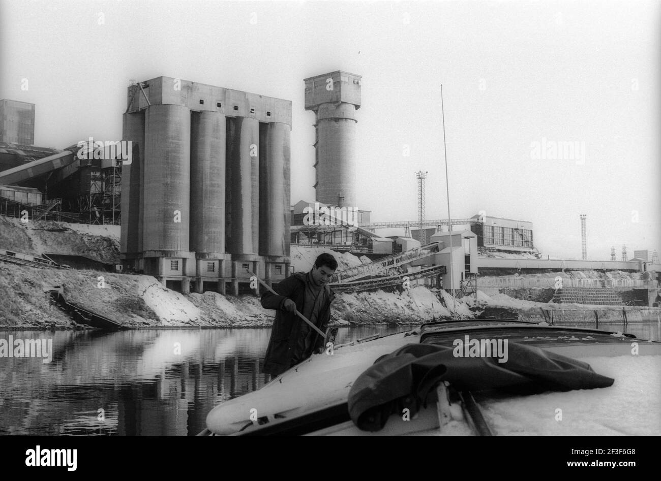 Man cleaning snow from river boat with a broom on the River Wear in front of Monkwearmouth Colliery Stock Photo