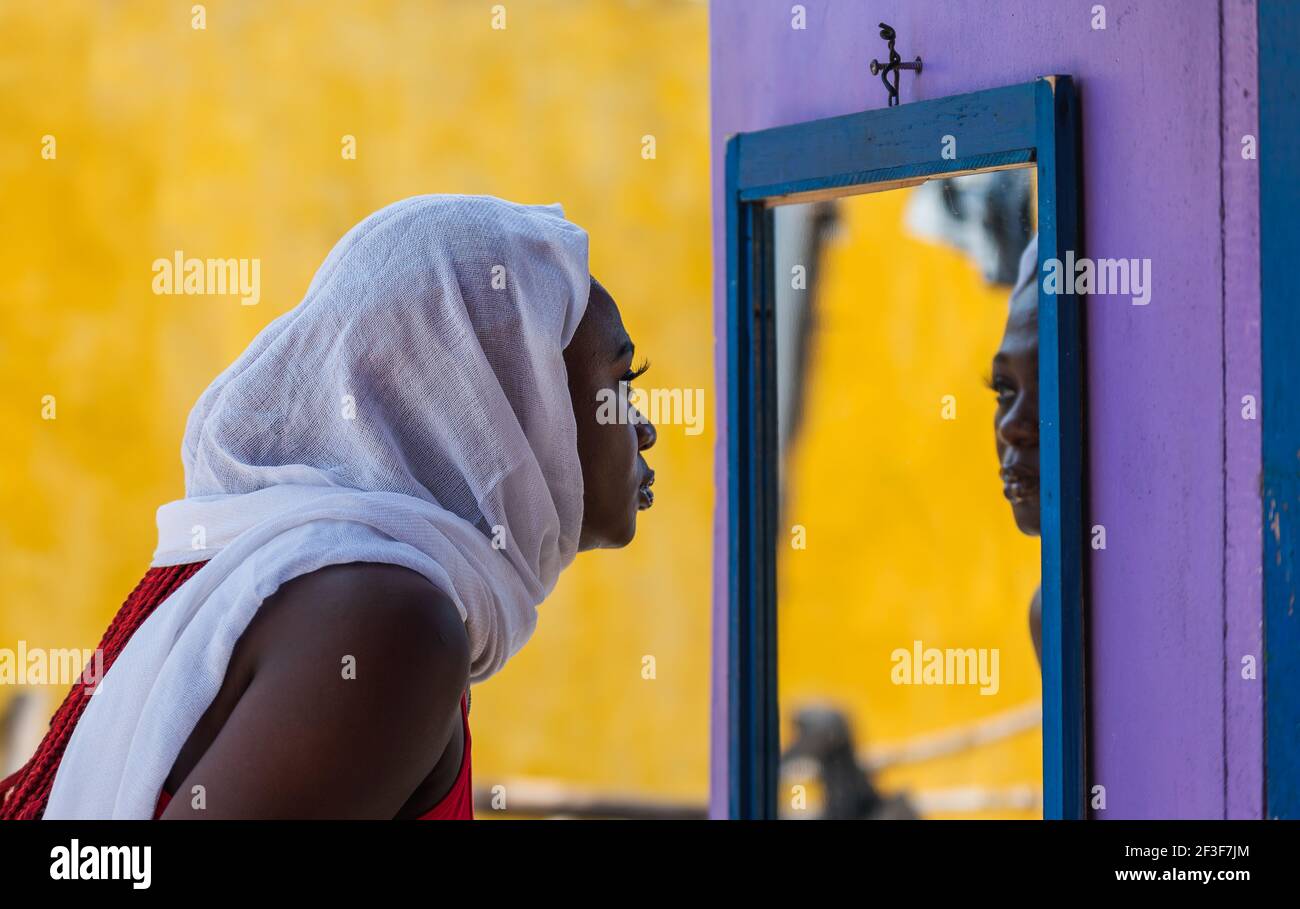 African Ghana woman standing in front of a mirror with a white shawl covering her hair Stock Photo