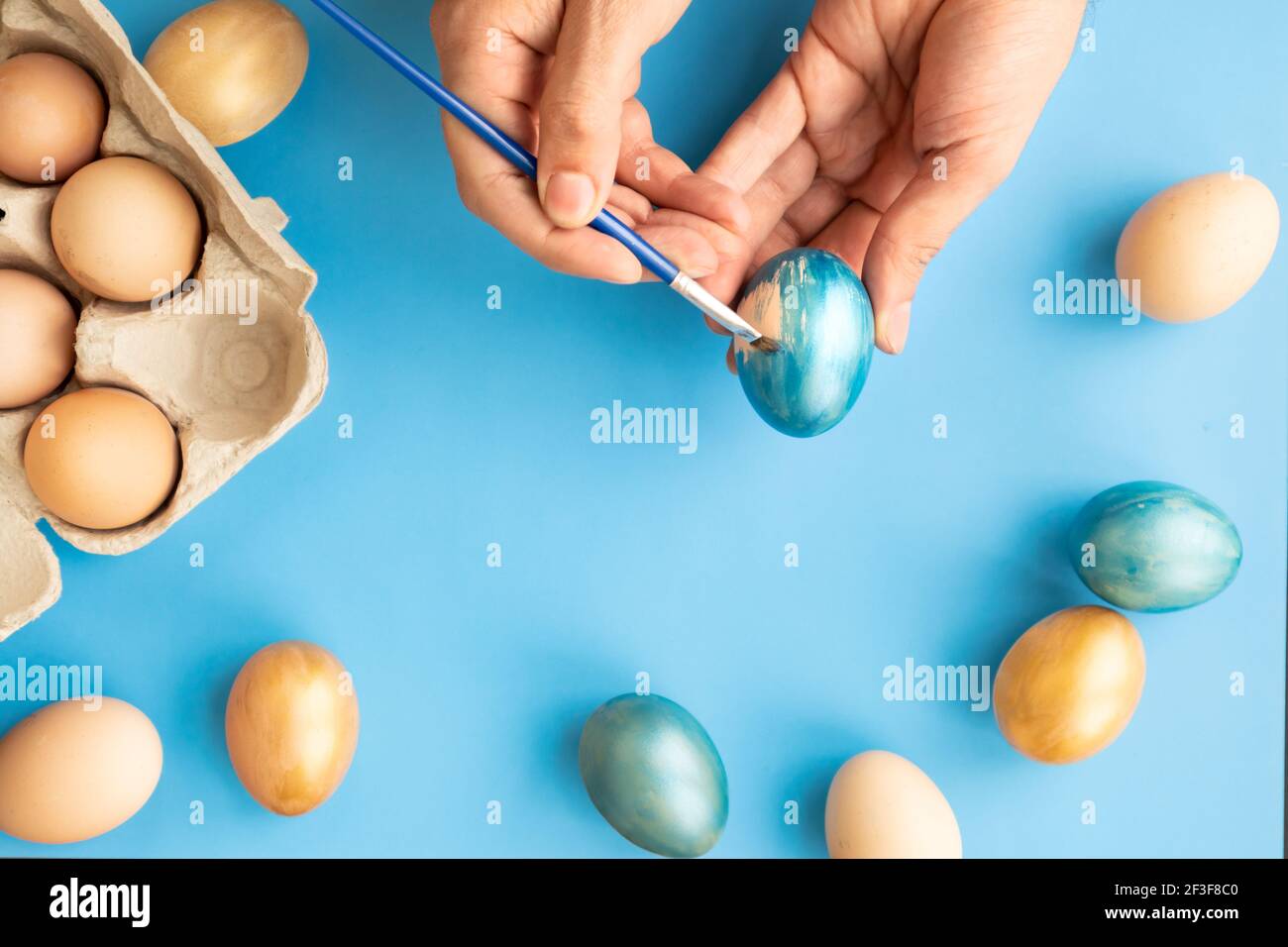 Preparing for Easter. Father painting Easter eggs on blue background. Easter day. Stock Photo